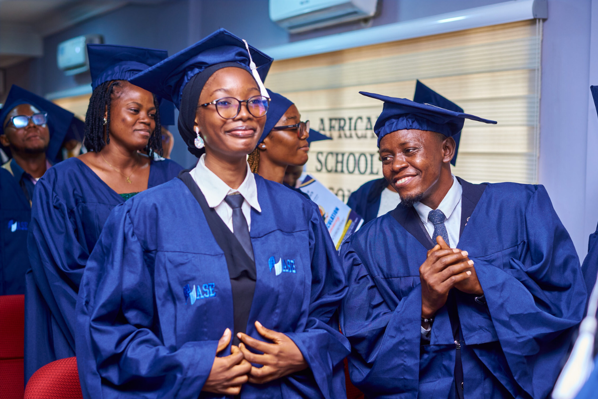 Students in graduation gowns smiling during a ceremony at the African School of Economics