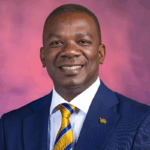 Portrait of Juma Nyamori, Head Teacher at Rusinga Schools in Nairobi, smiling in a formal suit against a soft pink and purple background