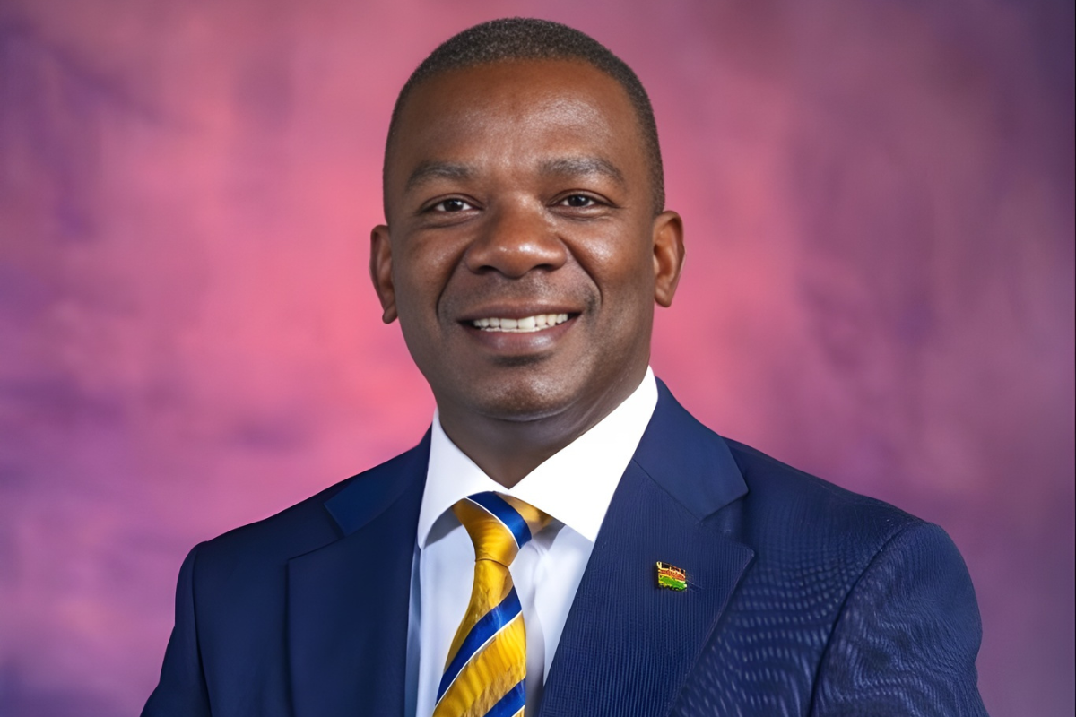 Portrait of Juma Nyamori, Head Teacher at Rusinga Schools in Nairobi, smiling in a formal suit against a soft pink and purple background