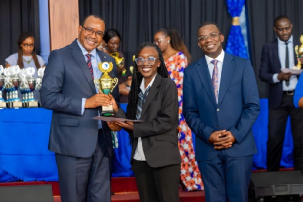 A student at Rusinga Schools receiving a trophy during an award ceremony, standing with school leaders on stage
