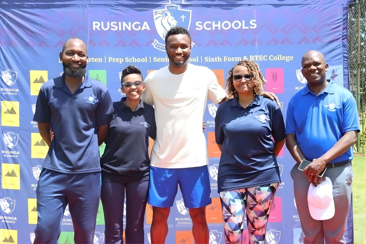 Group photo of Rusinga Schools staff and a student standing outdoors in front of a branded backdrop during a school event