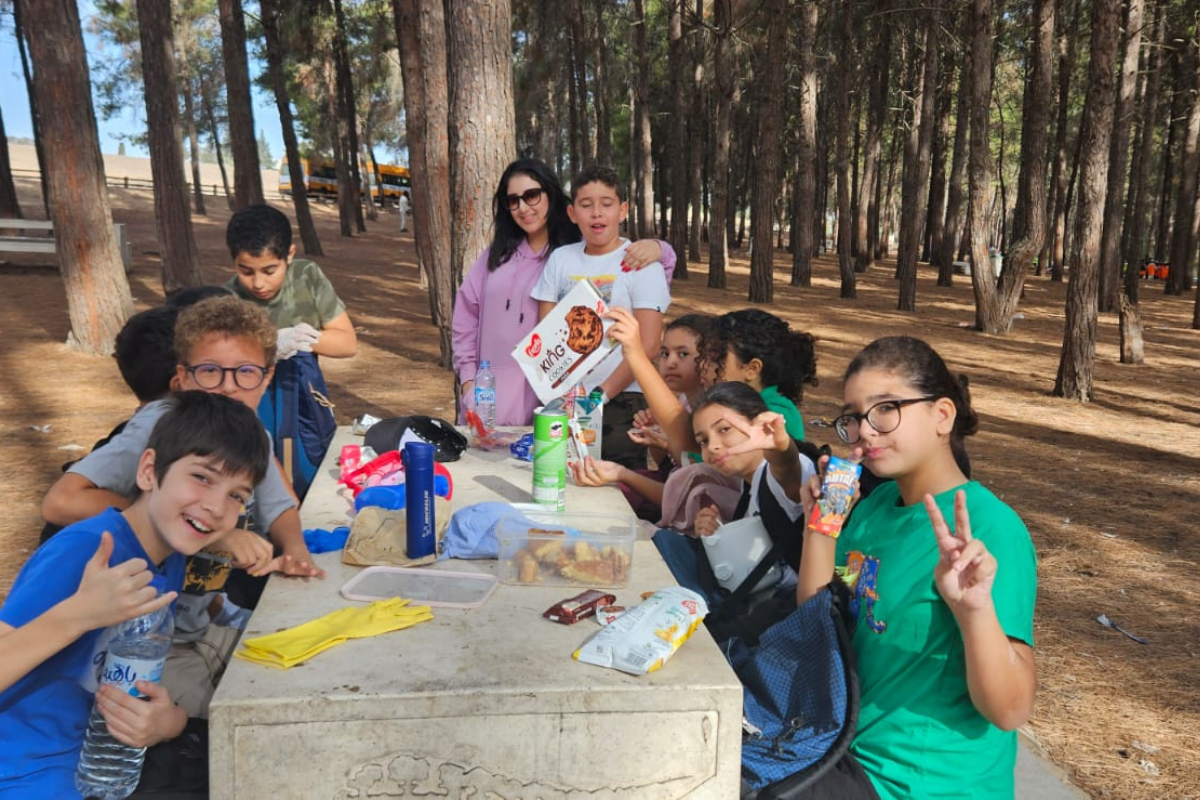 Pupils sitting at a picnic table during an outdoor school trip in a wooded area