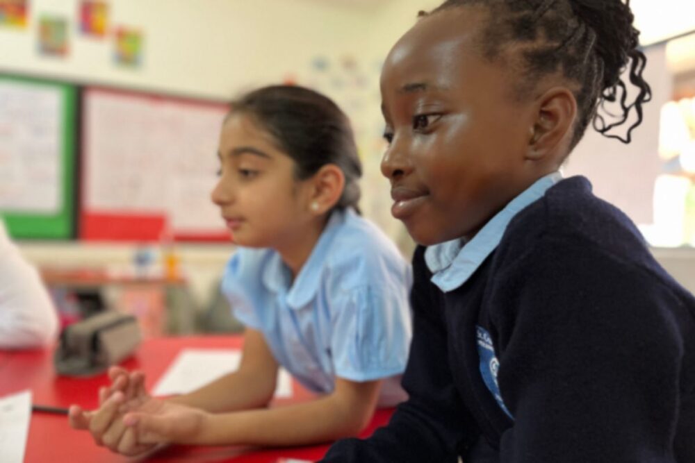 Two primary pupils sitting at a classroom table listening and thinking during a lesson