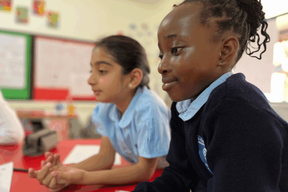 Two primary pupils sitting at a classroom table listening and thinking during a lesson
