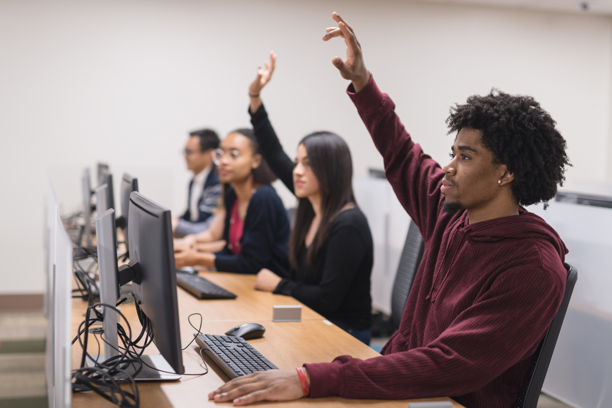 Students in an ICT classroom raising hands during a lesson